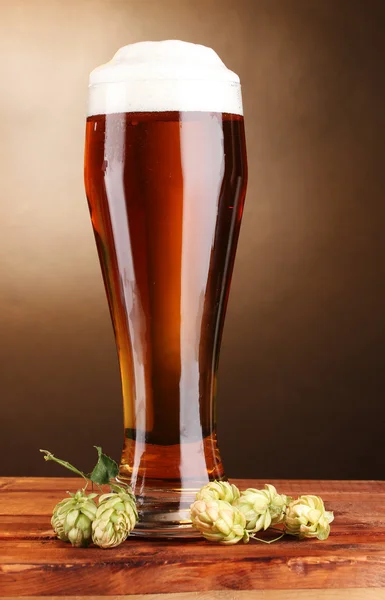 Cerveja em vidro e salto verde na mesa de madeira no fundo marrom — Fotografia de Stock