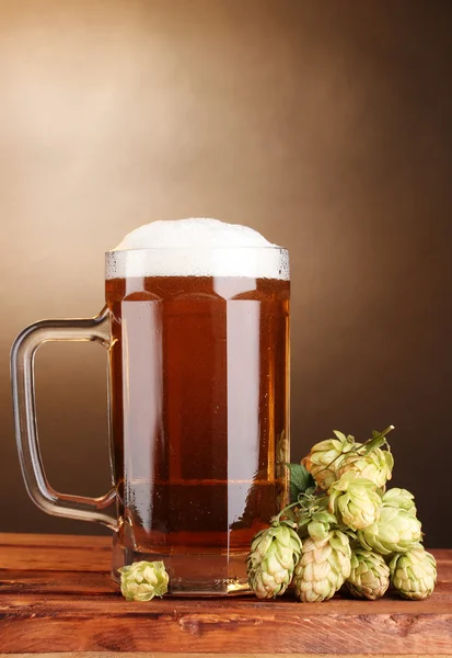 Bierkrug und grüner Hopfen auf Holztisch auf braunem Hintergrund — Stockfoto
