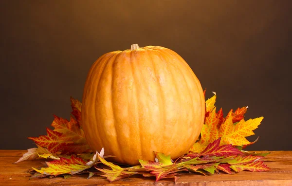 Zralá dýně a podzimní listí na dřevěný stůl na hnědé pozadí — Stock fotografie