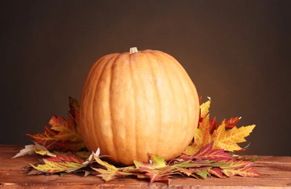 Dojrzałe dynia i liści jesienią na drewnianym stole na brązowym tle — Zdjęcie stockowe