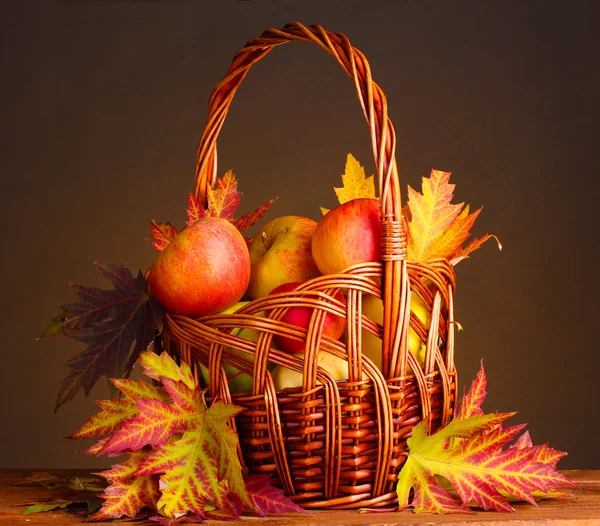 Beautiful autumn harvest in basket and leaves on brown background — Stock Photo, Image