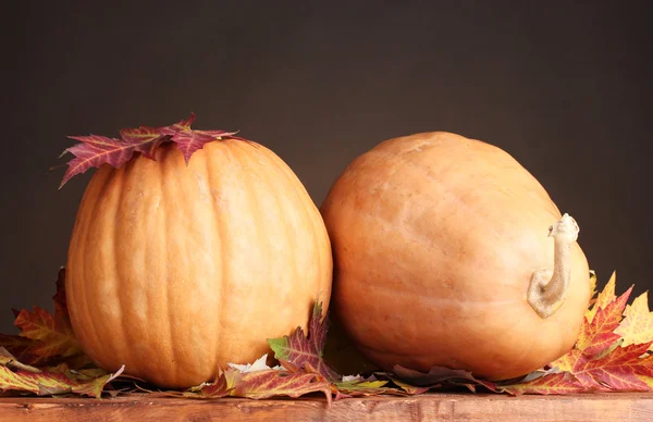 Two ripe pumpkins and autumn leaves on wooden table on brown background — Stock Photo, Image