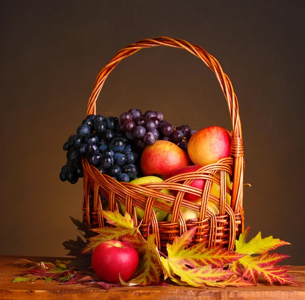 Beautiful autumn harvest in basket and leaves on brown background — Stock Photo, Image