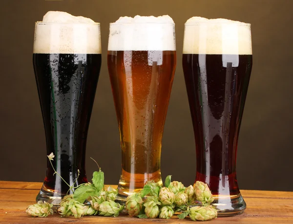 Τρία ποτήρια με διαφορετικές μπύρες και το λυκίσκο στο ξύλινο τραπέζι για καφέ backgro — Φωτογραφία Αρχείου