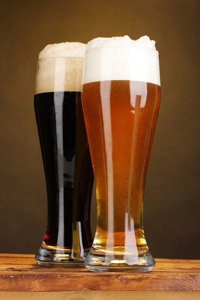 Zwarte en gouden bier in bril op houten tafel op bruine achtergrond — Stockfoto