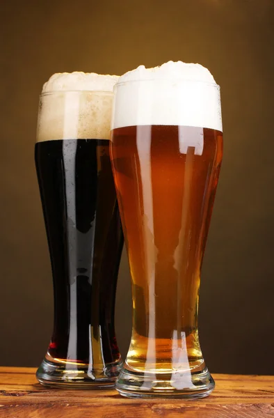 Cerveja preta e dourada em óculos na mesa de madeira no fundo marrom — Fotografia de Stock