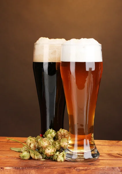 Svarta och gyllene öl i glasögon och hoppa på träbord på brun bak — Stockfoto