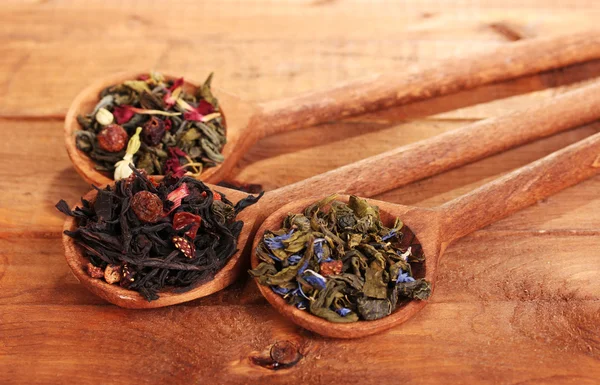 Различные виды зеленого и черного сухого чая в ложках на деревянном столе — стоковое фото