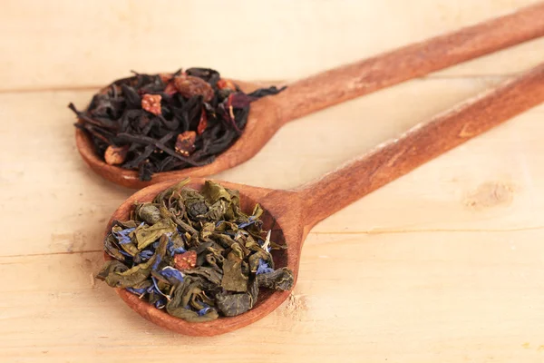 Diferentes tipos de chá seco verde e preto em colheres na mesa de madeira — Fotografia de Stock