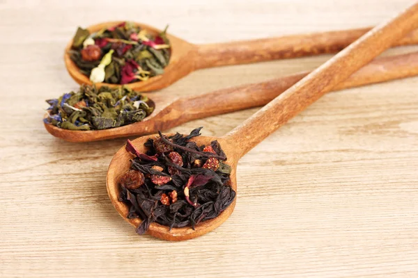 Diferentes tipos de té seco verde y negro en cucharas sobre mesa de madera —  Fotos de Stock