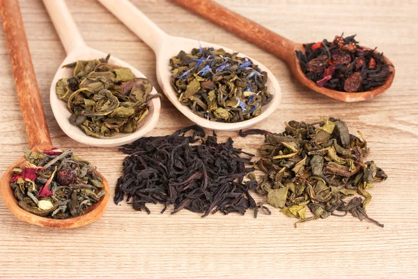 Diferentes tipos de chá verde e preto seco em colheres no fundo de madeira — Fotografia de Stock