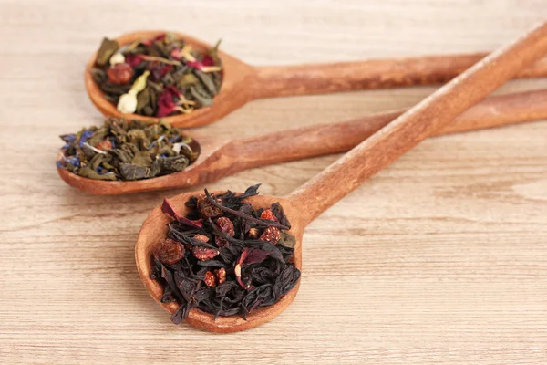 Verschillende soorten groene en zwarte droog thee in lepels op houten tafel — Stockfoto