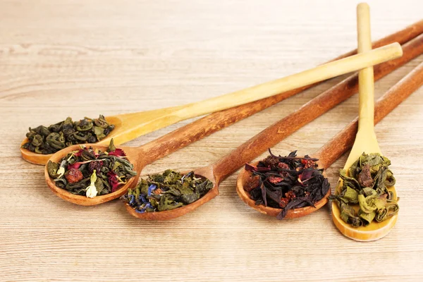 Different kinds of green and black dry tea in spoons on wooden table — Stock Photo, Image