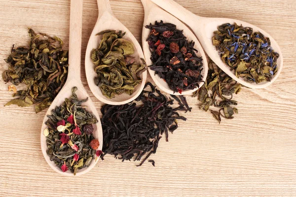Diversi tipi di tè verde e nero secco in cucchiai su sfondo di legno — Foto Stock