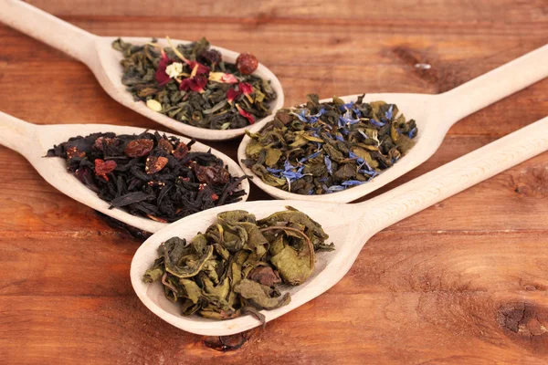 Verschillende soorten droge groene en zwarte thee in lepels op houten achtergrond — Stockfoto