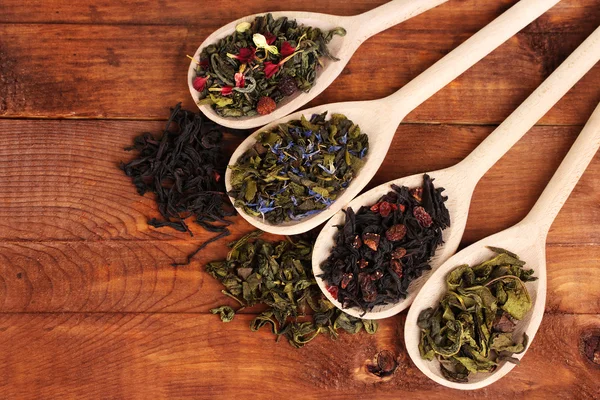Différents types de thé vert sec et noir dans des cuillères sur fond en bois — Photo
