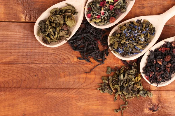 Verschillende soorten droge groene en zwarte thee in lepels op houten achtergrond — Stockfoto
