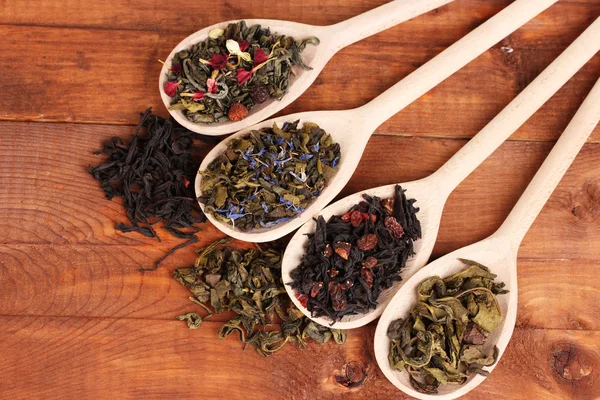 不同种类的干燥的绿茶和红茶中勺子木制背景上 — 图库照片