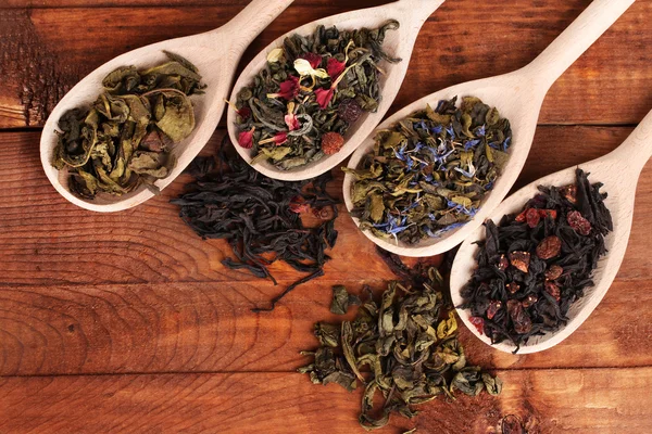 Diferentes tipos de chá verde e preto seco em colheres no fundo de madeira — Fotografia de Stock