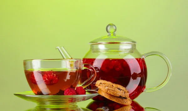 Black fruit raspberry tea in glass teapot and cup on green background — Stock Photo, Image