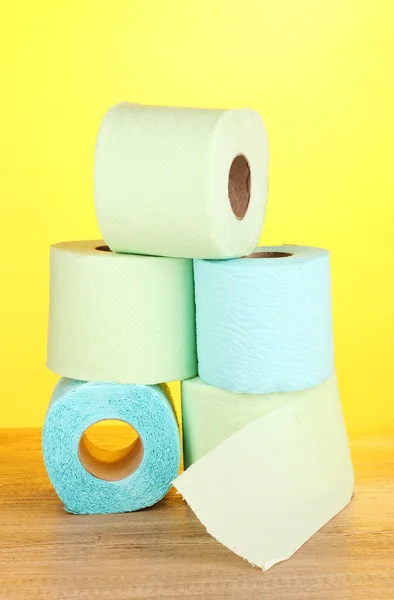 Green and blue rolls of toilet paper on wooden table on yellow background — Zdjęcie stockowe