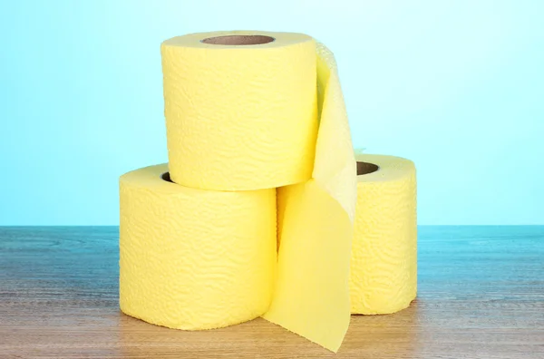 Three rolls of toilet paper on wooden table on blue background — Zdjęcie stockowe