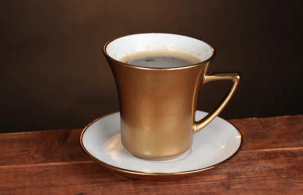 Zlatý šálek kávy na dřevěný stůl na hnědé pozadí — Stock fotografie