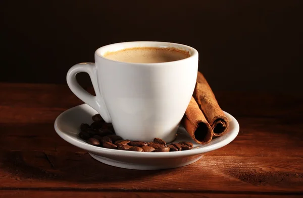 Cup with coffee, cinnamon and coffee beans on wooden table on brown backgr — Stock Photo, Image