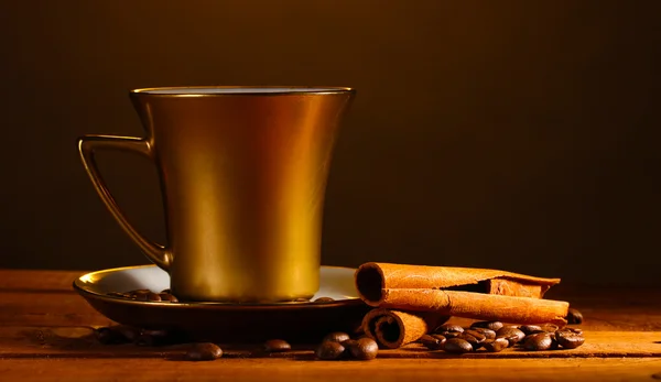 Copa de oro con café, canela y granos de café en la mesa de madera en marrón — Foto de Stock