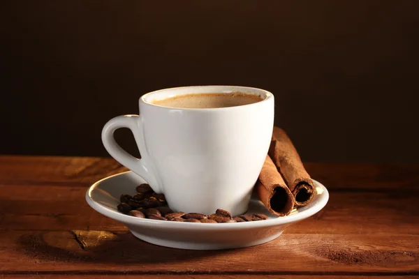Tazza con caffè, cannella e chicchi di caffè su tavolo di legno su dorso marrone — Foto Stock