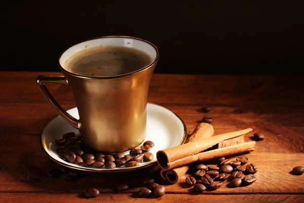 Cangkir emas dengan kopi, kayu manis dan biji kopi di atas meja kayu di atas cokelat — Stok Foto