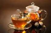 Glas Teekanne und Tasse mit exotischem grünem Tee auf Holztisch auf braunem Hintergrund