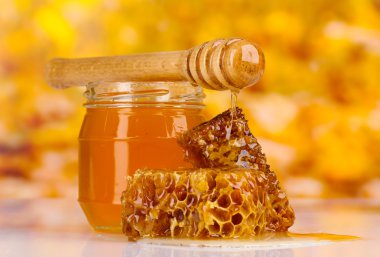 Jar of honey, honeycombs and wooden drizzler on yellow background clipart