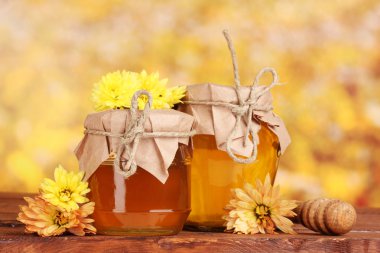 Two jars of honey and wooden drizzler on table on yellow background clipart