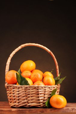 kahverengi backg üzerinde ahşap masa üstünde güzel bir sepet içinde yapraklarla mandalina