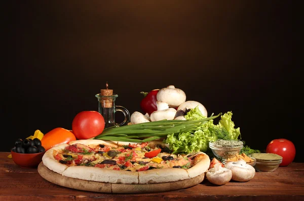 stock image Delicious pizza, vegetables and spices on wooden table on brown background