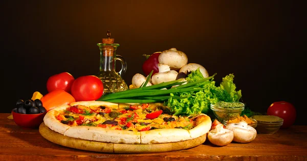 Heerlijke pizza, groenten en kruiden op houten tafel op bruine achtergrond — Stok fotoğraf