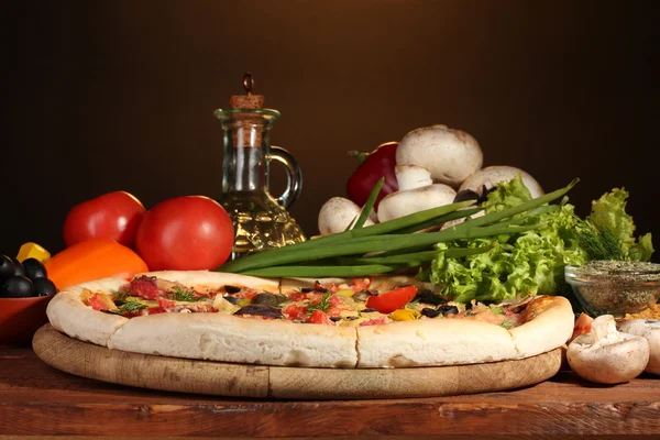 Délicieuse pizza, légumes et épices sur table en bois sur fond marron — Photo