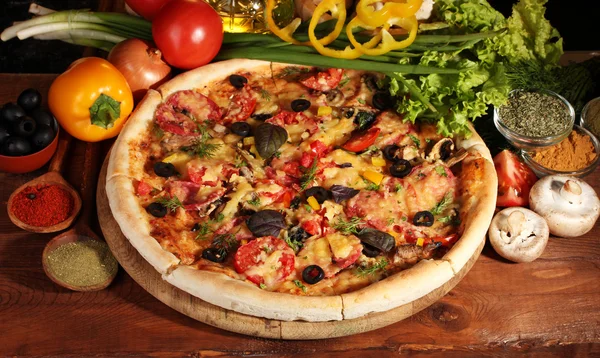 Deliciosa pizza, legumes e especiarias na mesa de madeira — Fotografia de Stock