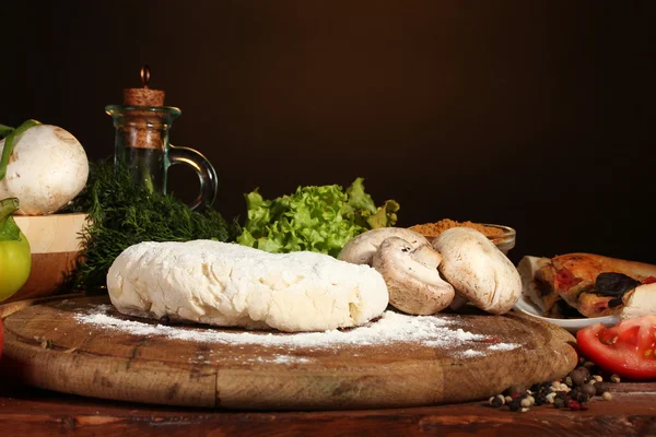 Смачне тісто для піци, спеції та овочі на дерев'яному столі на коричневому фоні — стокове фото
