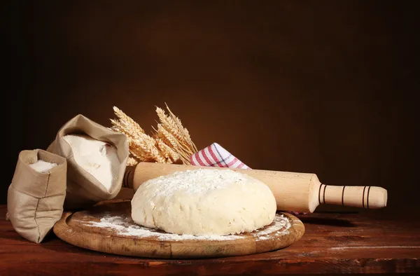 Ciasta i worki z mąką na drewnianym stole na brązowym tle — Zdjęcie stockowe