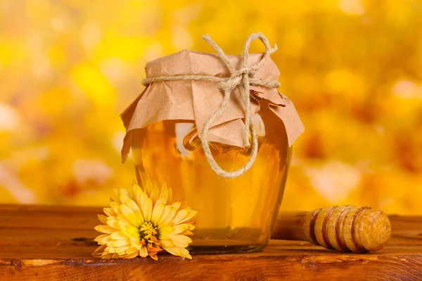 Jar of honey and wooden drizzler on table on yellow background — Stock Photo, Image