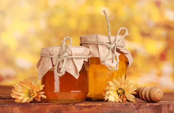 Két üveget, a méz és a fából készült drizzler a tábla, sárga háttér — Stock Fotó