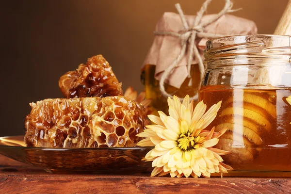 Dos tarros de miel, panales de miel y llovizna de madera en la mesa sobre fondo amarillo —  Fotos de Stock