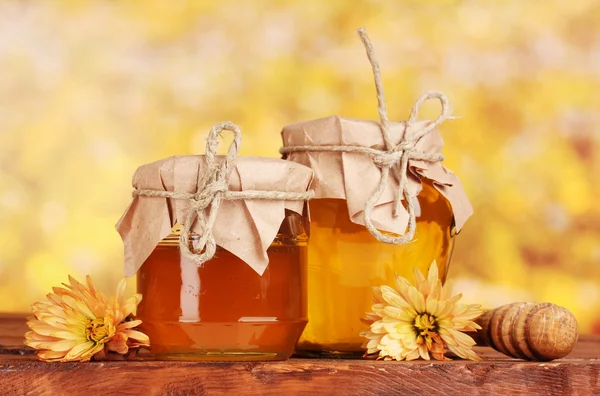 Dos frascos de miel y rociador de madera sobre la mesa sobre fondo amarillo — Foto de Stock