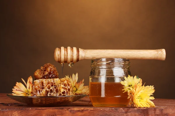 Jar of honey,honeycombs and wooden drizzler on table on yellow background — Stock Photo, Image