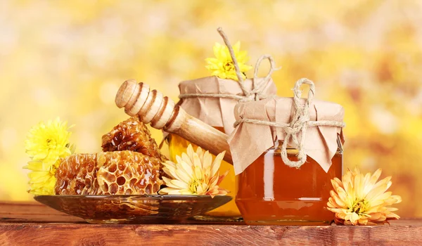 Twee potten van honing, honingraten en houten drizzler op tafel op gele backgro — Stockfoto