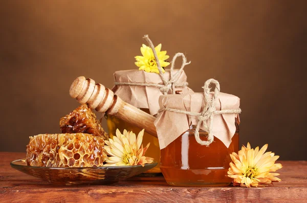 Deux pots de miel, des nids d'abeilles et un bruiteur en bois sur la table sur fond jaune — Photo