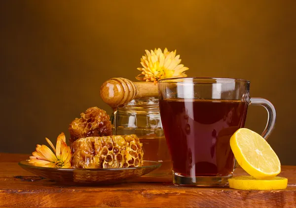 Honig, Zitrone, Waben und eine Tasse Tee auf einem Holztisch auf braunem Hintergrund — Stockfoto
