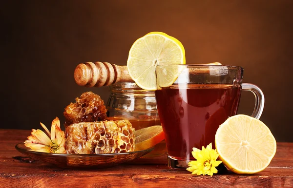 Stock image Honey, lemon, honeycomb and a cup of tea on wooden table on brown backgroun